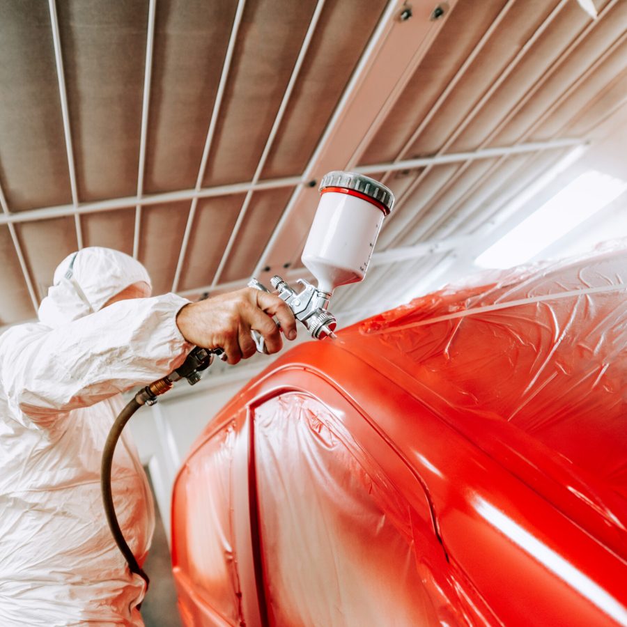 Close-up portrait of man with spray gun with red paint painting a car in special booth